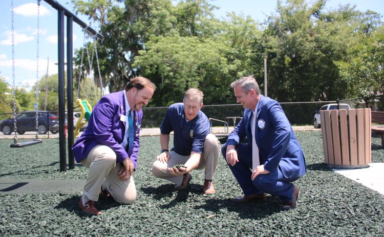 District Rotary Governor Dan Sulger (left), Rotary Club of Lake City President Jay Swisher (right) and Lake City Rotarian John Wheeler take a closer look at the rubber mulch that replaced sand at the Rotary Children’s Playground at downtown Wilson Park. (TONY BRITT/Lake City Reporter)