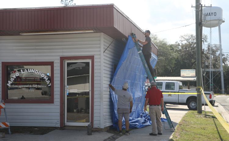 Mayo Laundromat owner Micah Hart staples a tarp to the outside of his business Tuesday afternoon after a semi crashed into the building, and pushed other vehicles through it, Tuesday morning. (MORGAN MCMULLEN/Lake City Reporter)