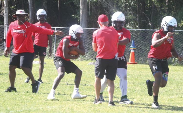 Fort White coach Demetric Jackson (left) hands the ball off to running back Maliki Clark (middle) during practice on May 1. (MORGAN MCMULLEN/Lake City Reporter)