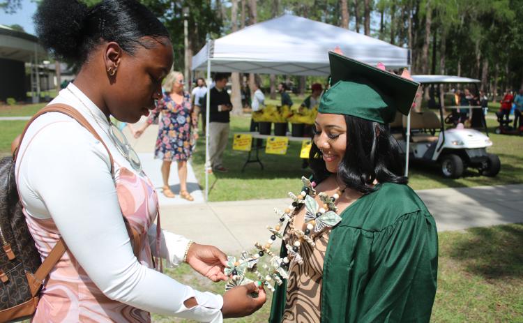 Gardine Raymond (from left) inspects the ‘money lei’ worn by her best friend Erika Maceira following Florida Gateway College’s 2023 Spring Commencement Ceremony on Friday morning. (TONY BRITT/Lake City Reporter)