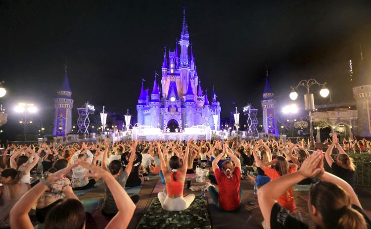 Walt Disney World cast members stretch at Cinderella Castle in a pre-dawn gathering during an annual team yoga session to commemorate International Yoga Day. (JOE BURBANK/Orlando Sentinel via AP)