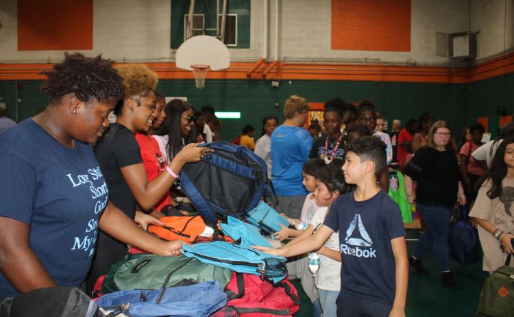 Volunteers hand out backpacks to children Sunday at the Community Barbers Giving Back To The Community Back-To-School event at Richardson Community Center. (TONY BRITT/Lake City Reporter)
