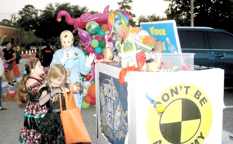 Xzailia Keown (from left), 8, checks her bag of candy as her sister, Nevaeh Keown, 9, gets candy from the DOT’s Crash Test Smarties during Tuesday night’s DOT Trunk or Treat event. (TONY BRITT/Lake City Reporter)