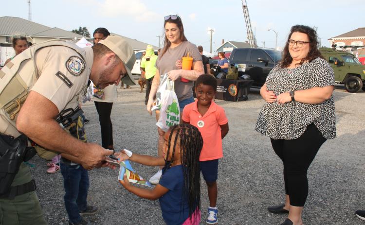 Luke Davenport, a Florida Fish and Conservation Commission officer, signs a coloring book for Ava Flores, 2, as Elias Flores, 4 and Chelsea Flores (far right) look on. (TONY BRITT/Lake City Reporter)
