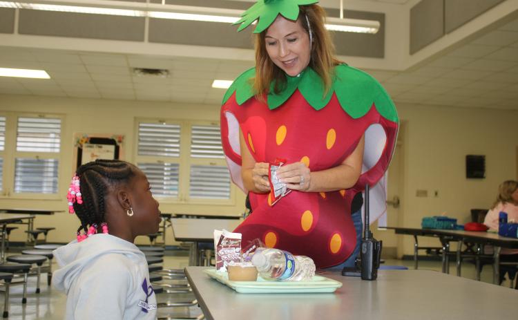 Westside Elementary School Principal Jennifer Saucer opens a carton of milk for a student Friday morning. Saucer was wearing the strawberry costume as part of National School Luncheon Week. (TONY BRITT/Lake City Reporter)