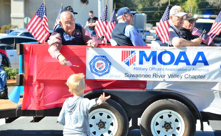 Vern Lloyd of Lake City hands a flag to a youngster who sprinted to catch up to the Military Officers Association of America float during the 2019 Veterans Day parade. (FILE)