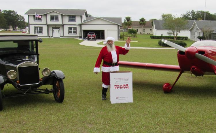 Mark Wiencek dresses as Santa next to a Cessna and a box of presents for Toys for Tots. (TONY BRITT/Lake City Reporter)