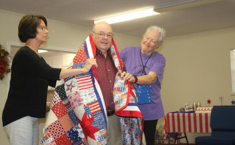 Terry Demott (center), a US Army veteran who served in the Vietnam War, is draped by Dianne Shepherd and Fran Vogt on Wednesday morning at a Quilts of Valor ceremony.  The quilts were made by the Lady of the Lake Quilt Guild members. (TONY BRITT/Lake City Reporter)
