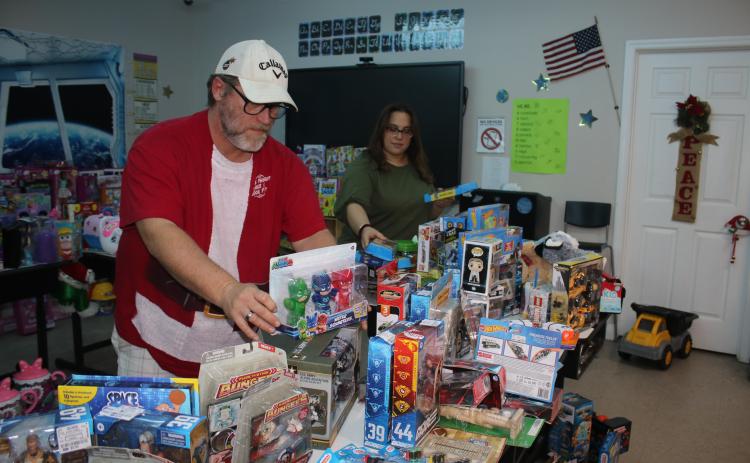 John ‘Lit’ Cole (from left), Kids Feeding Kids president, and Sharon Simpkins set up toys for the Kids Feeding Kids Christmas event. (TONY BRITT/Lake City Reporter)