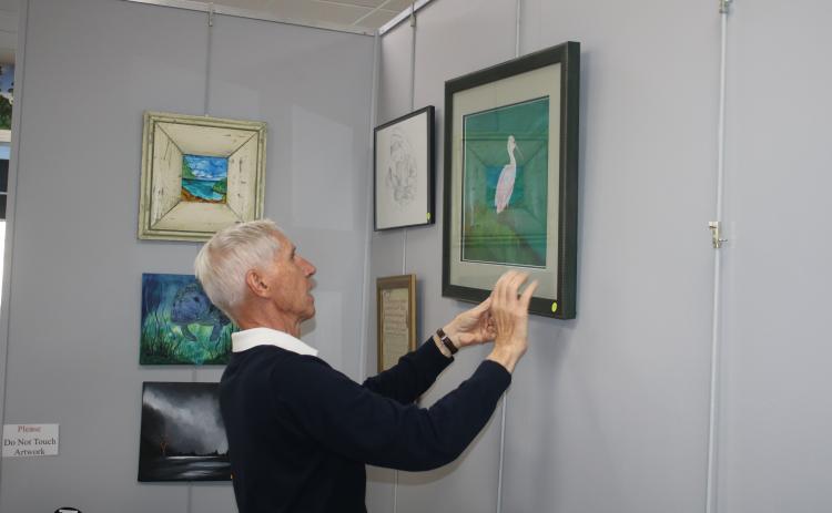 Jim Riley, former president of the Art League of North Florida and the Gateway Art Gallery, hangs up an entry into the 10th annual winter art show on Saturday. (TONY BRITT/Lake City Reporter)