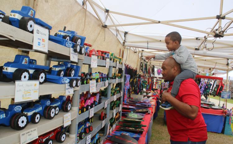 Keaven Jones gives Kaden Jones, 2, a ride on his shoulders as the youngster points out wooden cars in a vendor’s both on Friday afternoon at the 45th Annual Olustee Festival. (TONY BRITT/Lake City Reporter)