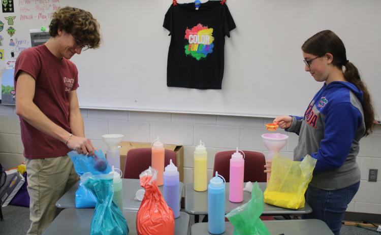 Brody Crews (left) and Isabel Heeke, Fort White High School National Honor Society club officers, fill dispensers with paint for the club’s color fun run that will take place on Saturday at the school’s football stadium. (TONY BRITT/Lake City Reporter)