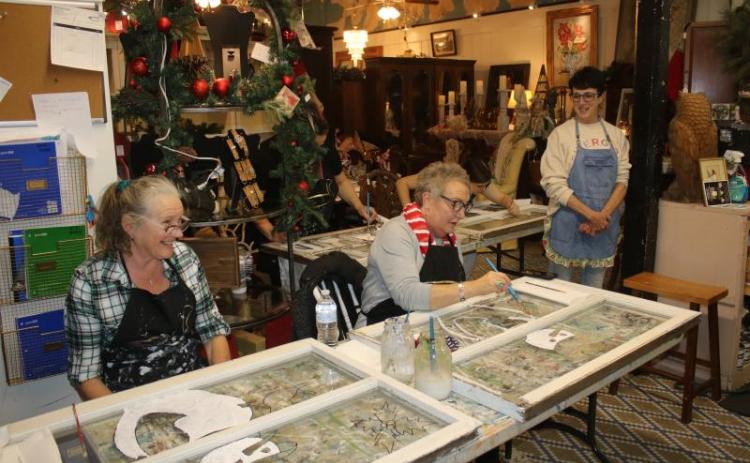 Tina Teasley (from left) and Tami Saperstein paint a snowman on window panes during an art class at the Blue Goose Studio during December’s Art Stroll. (FILE)