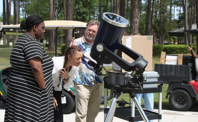 Jessica Ervienn (middle) squints as she looks through a telescope to watch Monday’s solar eclipse as she gets tips from FGC physics professor James Givviens. (TONY BRITT/Lake City Reporter)