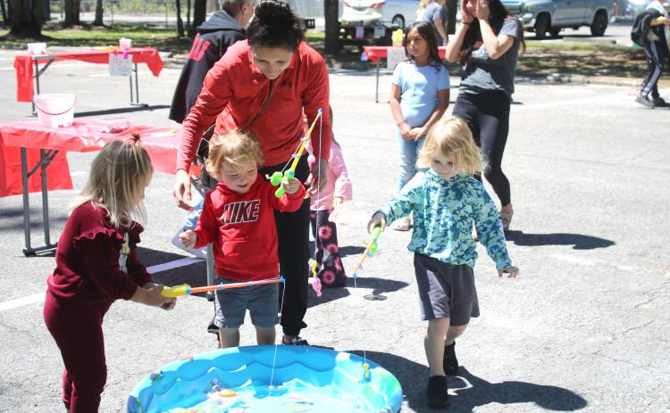Aniya Woodcock (from left), 4, Khalil Williams, 2, and Parker Pemberton, 4, get help from Katie Stewart as the youngsters play a game attempting to catch plastic fish at the Spring Family Fun Day at Ichetuckee Springs State Park on Saturday. (TONY BRITT/Lake City Reporter)