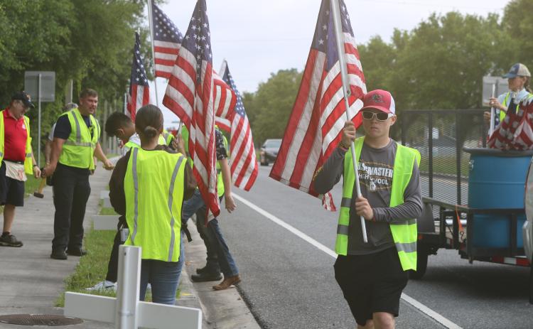 Pheonix Polansky, a cadet with the Columbia High School JROTC program, carries a flag that was later added to a cross for the Flags for Heroes display on State Road 47. (TONY BRITT/Lake City Reporter)
