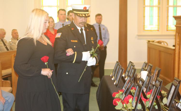 Julie Boozer, accompanied by Lt. Greg Sund, prepares to place a rose at the base of her father’s portrait during Tuesday’s Public Safety Memorial. Boozer’s father, Dwight, was Lake City’s assistant fire chief. (TONY BRITT/Lake City Reporter)