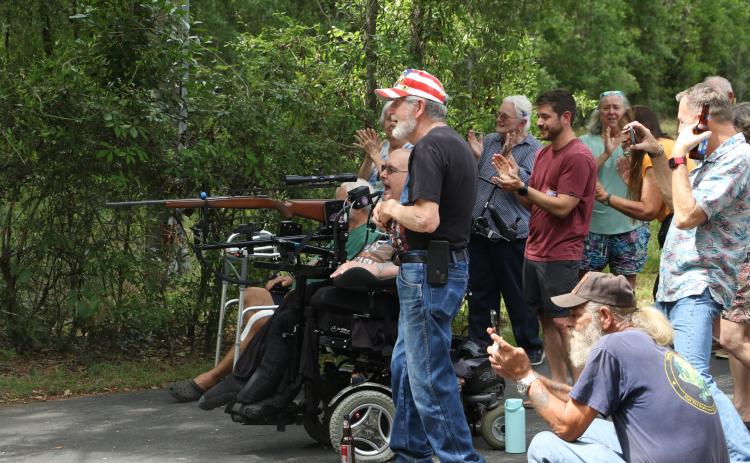Pete Herrick, surrounded by friends and family, reacts after firing a breath-powered .308 rifle to set off a stack of cakes filled with Tannerite binary explosives Saturday during his ‘Alive Party.’ Herrick, a Fort White man, was seriously injured during Operation Iraqi Freedom 20 years ago today. (MORGAN MCMULLEN/Lake City Reporter)