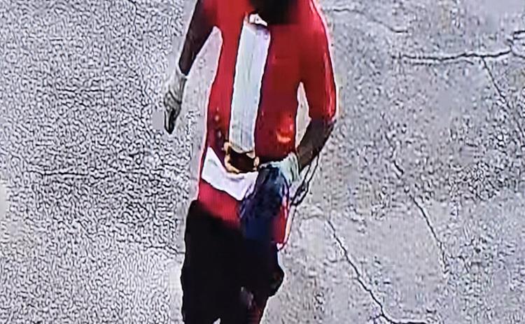 Gary Hollie, wearing a Halloween-style mask and a ‘Santa’ T-shirt, runs from the Dollar General on SW Main Boulevard after an armed robbery at the store on June 12. (COURTESY)