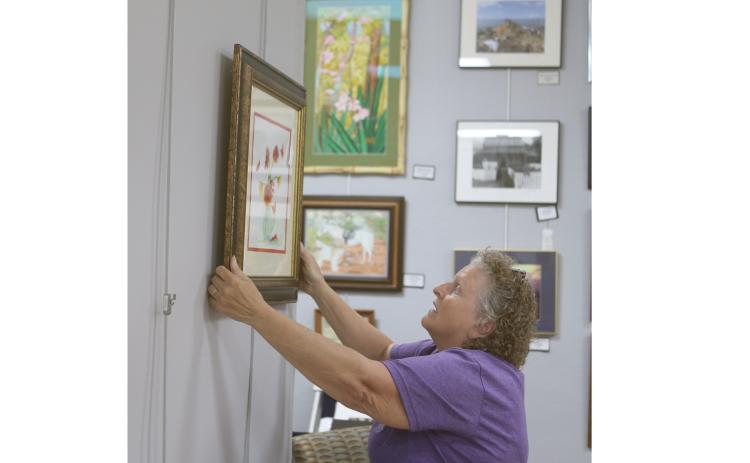 Janet Hans, an artist and a volunteer jewelry-making instructor at the Gateway Art Gallery, hangs artwork for the Gallery’s Christmas in July reception today. (TONY BRITT/Lake City Reporter)