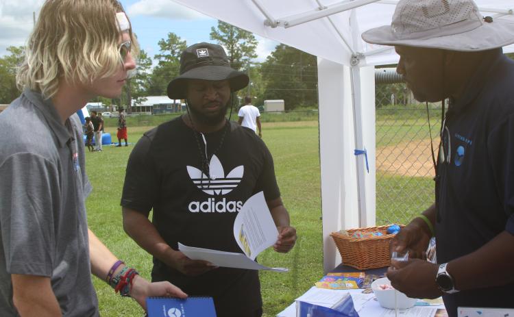 Samuel Jeter (from left) and Carlos Scippio collect information and school materials from Travis George at the Project Cope vendor booth during the inaugural Unity Community Day at Richardson Community Center. (TONY BRITT/Lake City Reporter)