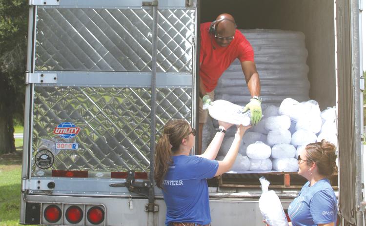 Justice Kite (from left) gets a bag of ice from Darius Parker as she and Cassie Burke, Vystar employees, prepare to give the ice to southern Columbia County residents who were left without  electricity following Hurricane Debby. (TONY BRITT/Lake City Reporter)