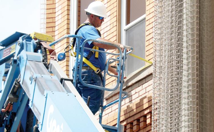A worker measures a window on the outside of Lake City Hall on Tuesday as work begins to determine what is causing issues with the bricks on the historic building so the protective netting can be removed. (TONY BRITT/Lake City Reporter)