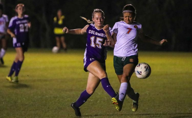 Columbia's Zoe Bulock (15) gets a shot off while tightly defended by Eastside's Kikyo Johnson (7) during Tuesday's match. (BRENT KUYKENDALL/Lake City Reporter)