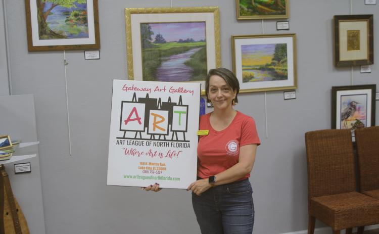 Sheila Carr, Gateway Art Gallery curator, is pictured with an Art League sign after they closed on purchasing their downtown building Thursday. (TONY BRITT/Lake City Reporter)