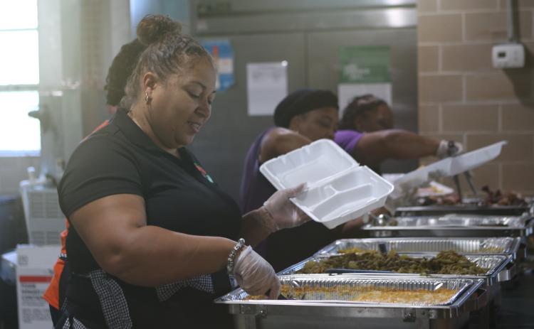 Nicole Callum, a Richardson Community Center board member, serves up macaroni and cheese for a to-go box during the center’s Friends in Need Thanksgiving Dinner on Saturday. (TONY BRITT/Lake City Reporter)