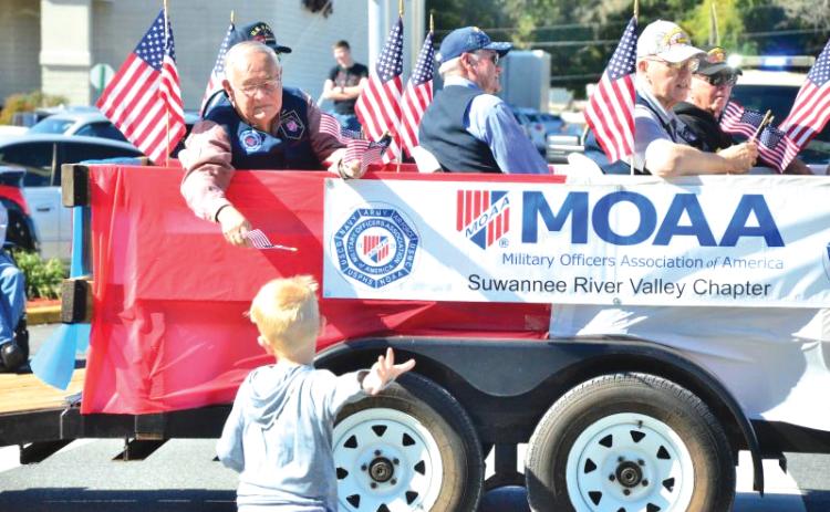 Vern Lloyd of Lake City hands a flag to a youngster who sprinted to catch up to the Military Officers Association of America float during the 2019 Veterans Day parade. (FILE)