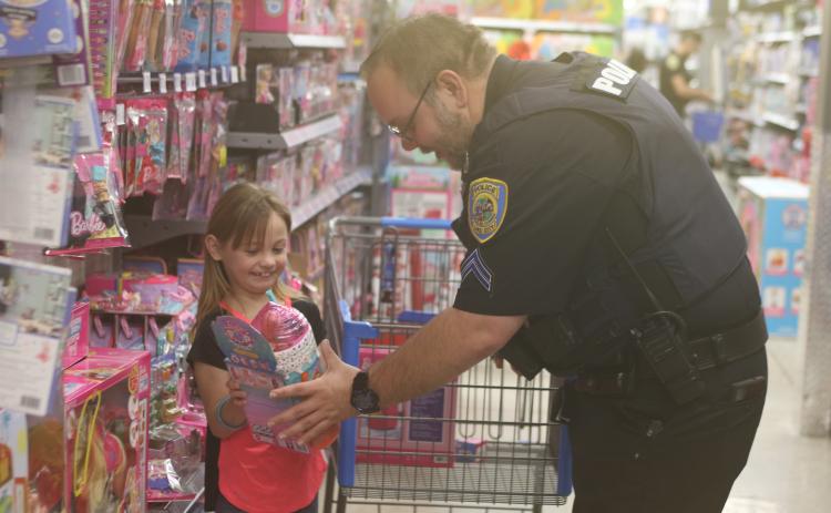 Paisley Daniels (left) is all smiles as she shows Lake City Police Department officer Brandon Rose an item she has selected for a Christmas gift, during LCPD’s Shop With A Cop event on Wednesday morning at Walmart. (TONY BRITT/Lake City Reporter)