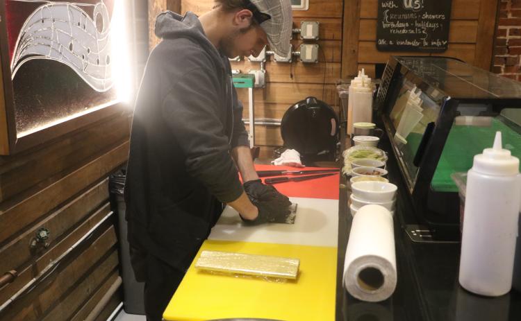 Tyler Hilton, a sushi chef at The Tavern, rolls up some sushi Friday afternoon as part of the Ribs and Rolls lunch special. Among that lunch menu is the Cowboy Roll, which is made with brisket, cream cheese, barbecue sauce and green Sriracha and then is deep fried. (MORGAN MCMULLEN/Lake City Reporter)