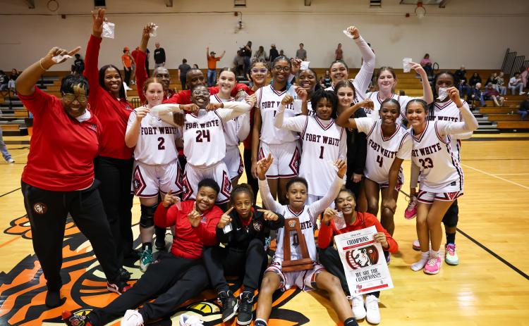 The Fort White girls basketball team celebrates with the District 6-R trophy after defeating Trenton on Saturday night. (JACK HOWDESHELL/Lake City Reporter)