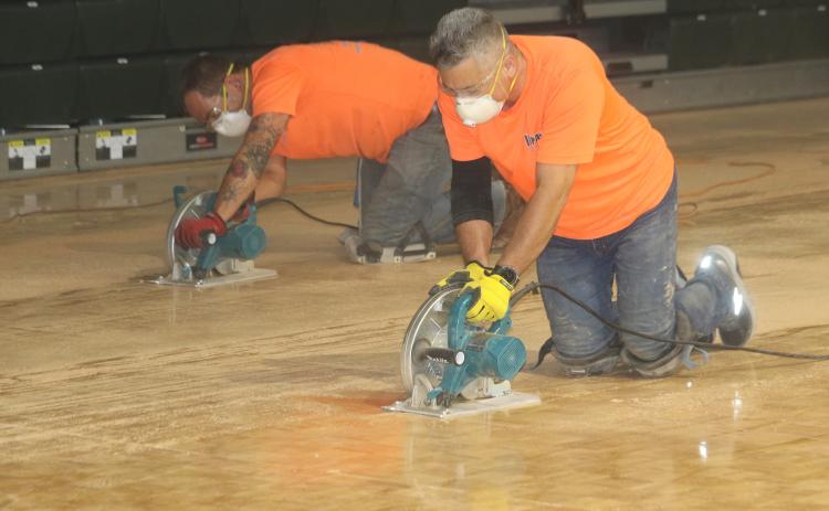 Frank Roque (foreground) and Corey Watkins of Impact Sport Surfaces Inc., use saws to cut FGC’s old parquet basketball court. (TONY BRITT/Lake City Reporter)