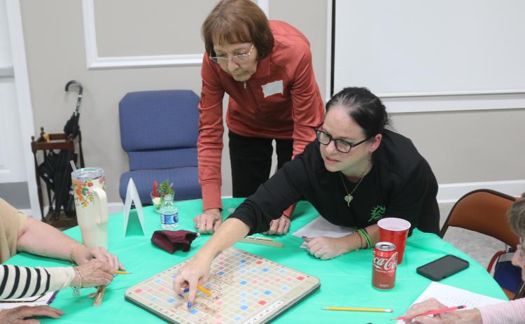 Linda Jansson (left) looks on as her Scrabble partner, Theresa DePasquaoe, places letter tiles on the Scrabble board during the championship round of the Lake City Garden Club’s Scrabble Tournament fundraiser. The pair won the tournament. (TONY BRITT/Lake City Reporter)