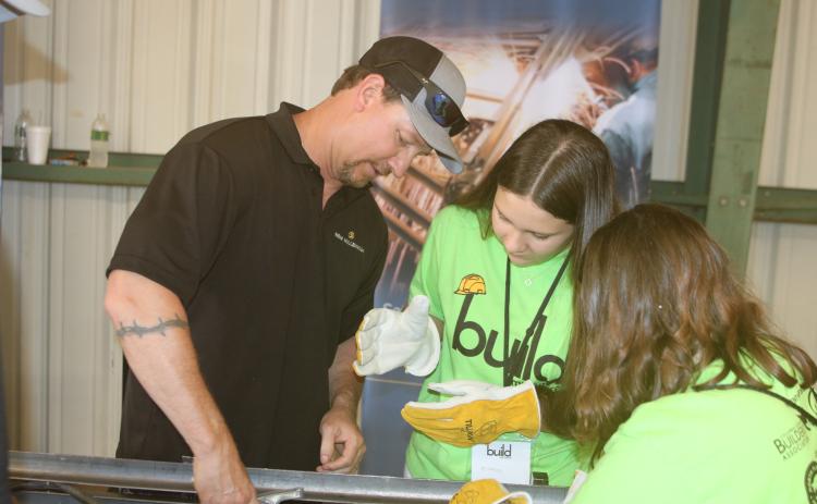 Gerard Gardner (clockwise from left), a New Millennium employee, shows Baker County High School students Mikayla Evans and Brooklyn Welsh how to work on building supports. (FILE)