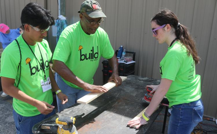 Angel Gomez, a Columbia High School student, gets tips on sanding wood from Monty Ashby, as Gomez and Kiley Morrison sand wood to make beds for the Sleep in Heavenly Peace program. The students manufactured the beds during the Build My Future event on Wednesday morning at the Florida Gateway Fairgrounds. (TONY BRITT/Lake City Reporter)