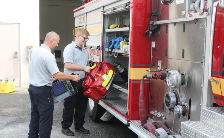 Columbia County Fire Rescue employee Jake Doyle (left) holds a cardiac monitor as Justin Ingle loads an Advanced Life Saving bag onto a fire engine at Station 43 on Friday morning. (TONY BRITT/Lake City Reporter)