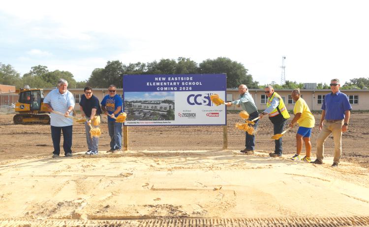 Keith Couey (from left), Hunter Peeler, Roger Little, Keith Hudson, Fred Gaylard, Scharlotte Stewart and Todd Widergren toss soil to commemorate the official beginning of construction of the new Eastside Elementary School. The groundbreaking ceremony took place on Wednesday morning amid construction crews beginning the first stages of demolition work at the school. (TONY BRITT/Lake City Reporter)