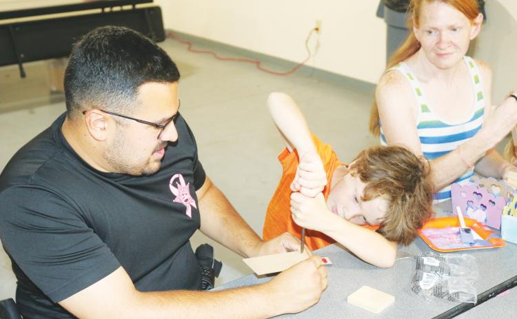 Columbia County School Resource Deputy Tony Geurra helps Negan Barker, 8, with his wood working skills. (TONY BRITTLake City Reporter)