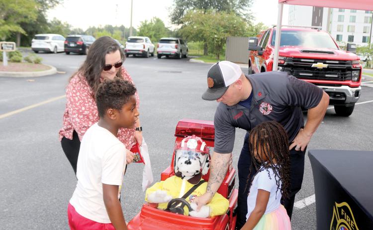 Elias Flores (clockwise from left), 6, Chelsea Flores, Lake City Firefighter Dustin Alford and Ava Flores, 4, play with Patches, a fire department remote controlled vehicle during the Fire Rescue N’ Cones event on Monday. (TONY BRITT/Lake City Reporter)