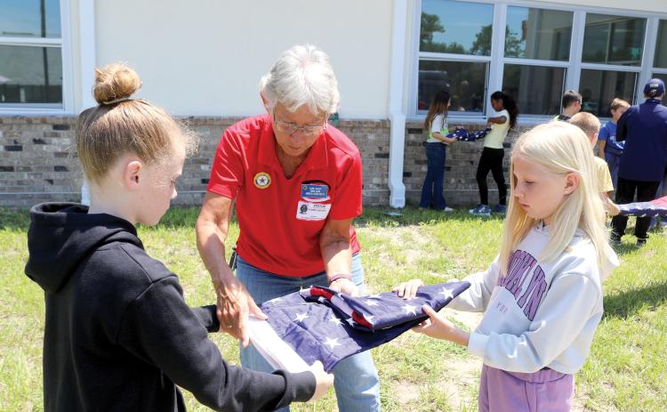 Elaine Lagasse, a member of the American Legion Post 57 Honor guard, helps a pair of Fort White Elementary School students fold a flag during a flag etiquette lesson Wednesday. (TONY BRITT/Lake City Reporter)