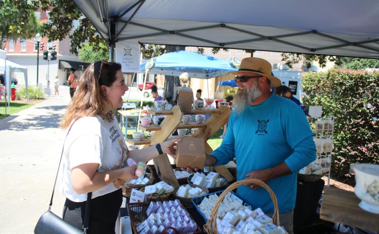 A shopper at a previous market event in downtown Olustee Park buys soap from the Kinghorn Farms booth. The City of Lake City’s Growers and Makers Market returns downtown Saturday. (FILE)