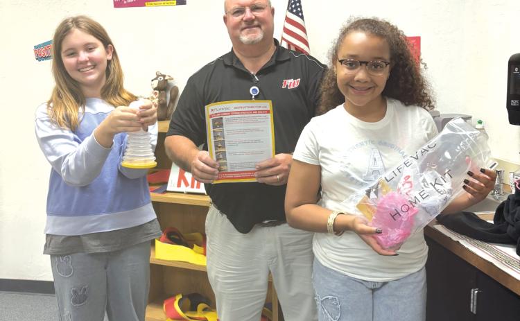 Charlie Stermer (from left) holds a LifeVac Airway Clearance Device while  standing with Ed Carter, Fort White Elementary School principal, and Aubrie Brown, holds a bag with another of the devices. (COURTESY)