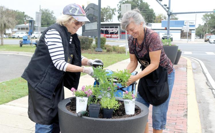 Judy MacGrath (from left) and Sonya Rossin, members of the Lake City Garden Club, take flowers out of their planters to add them to the city’s planter. (TONY BRITT/Lake City Reporter)