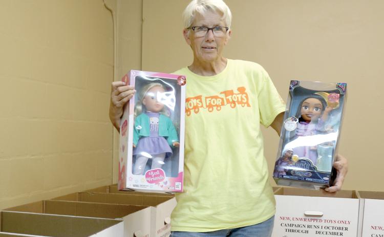 Inga Dwyer, the Toys for Tots coordinator for Columbia and Lafayette counties, holds up a pair of dolls at her new office for this year at 819 SW Alachua Avenue in Lake City. (TONY BRITT/Lake City Reporter)