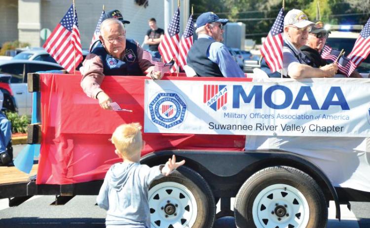 Vern Lloyd of Lake City hands a flag to a youngster who sprinted to catch up to the Military Officers Association of America float during the 2019 Veterans Day parade. (FILE)