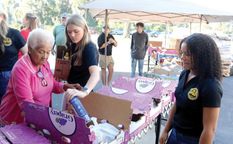Catholic Charities volunteers Carrie Alexander (clockwise from left), Madeline Moore and Amani Tunsil add items to boxes that were given to local families for the annual Catholic Charities Thanksgiving Basket giveaway, which was held Thursday. (TONY BRITT/Lake City Reporter)