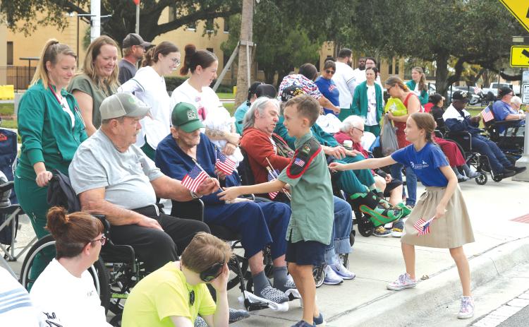 A pair of youngsters hand out American flags to veterans and others during Saturday’s Veterans Day parade in Lake City. (TONY BRITT/Lake City Reporter)